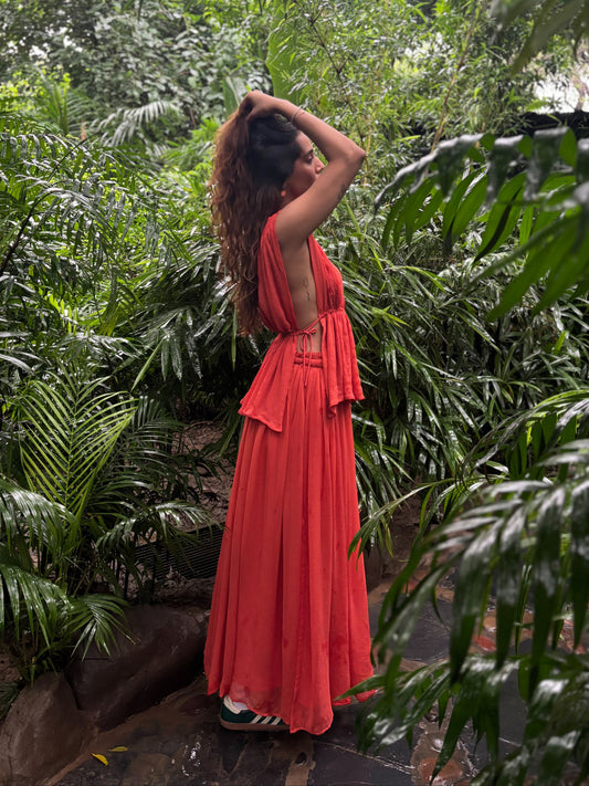 Woman in a red dress standing amidst lush green foliage. RUH Agni Silk Set in orange rust – luxury slow fashion coord crafted by artisans in Chandigarh, blending Indian heritage with modern design.
