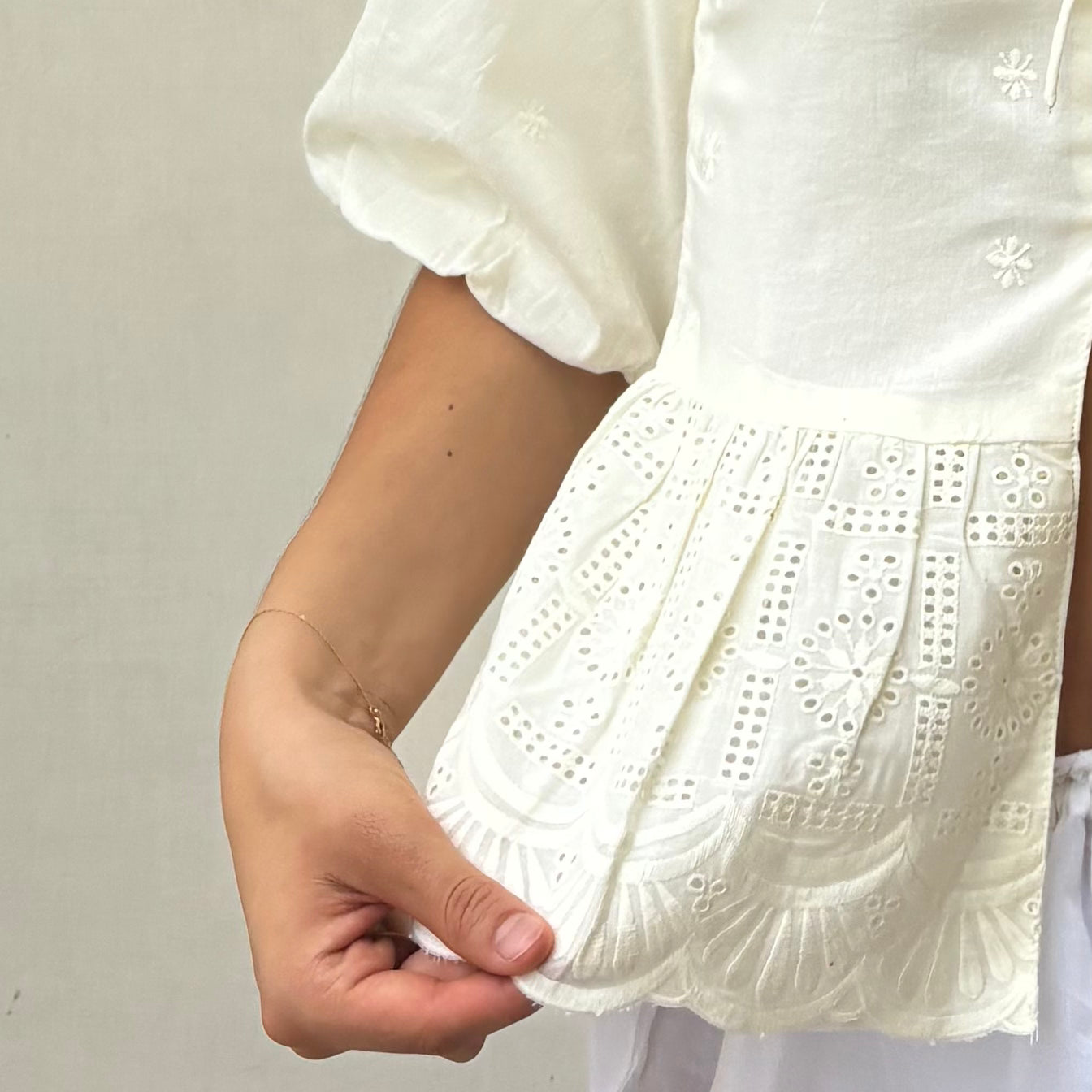 Close-up of a white blouse with intricate lace detailing on a plain background. Detail of RUH Muse Blouse bow ties and puff sleeves, inspired by Indian heritage reimagined for global wardrobes.