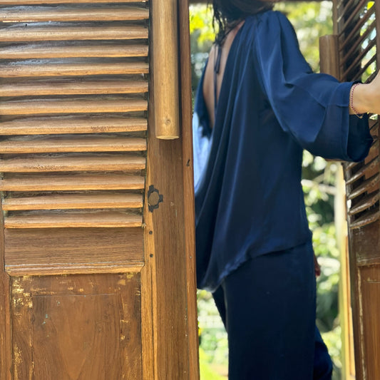Person in doorstep, the draped cowl-back satin silk top from RUH Aurora Set is emphasised, slow fashion luxury with cultural fusion aesthetics. 