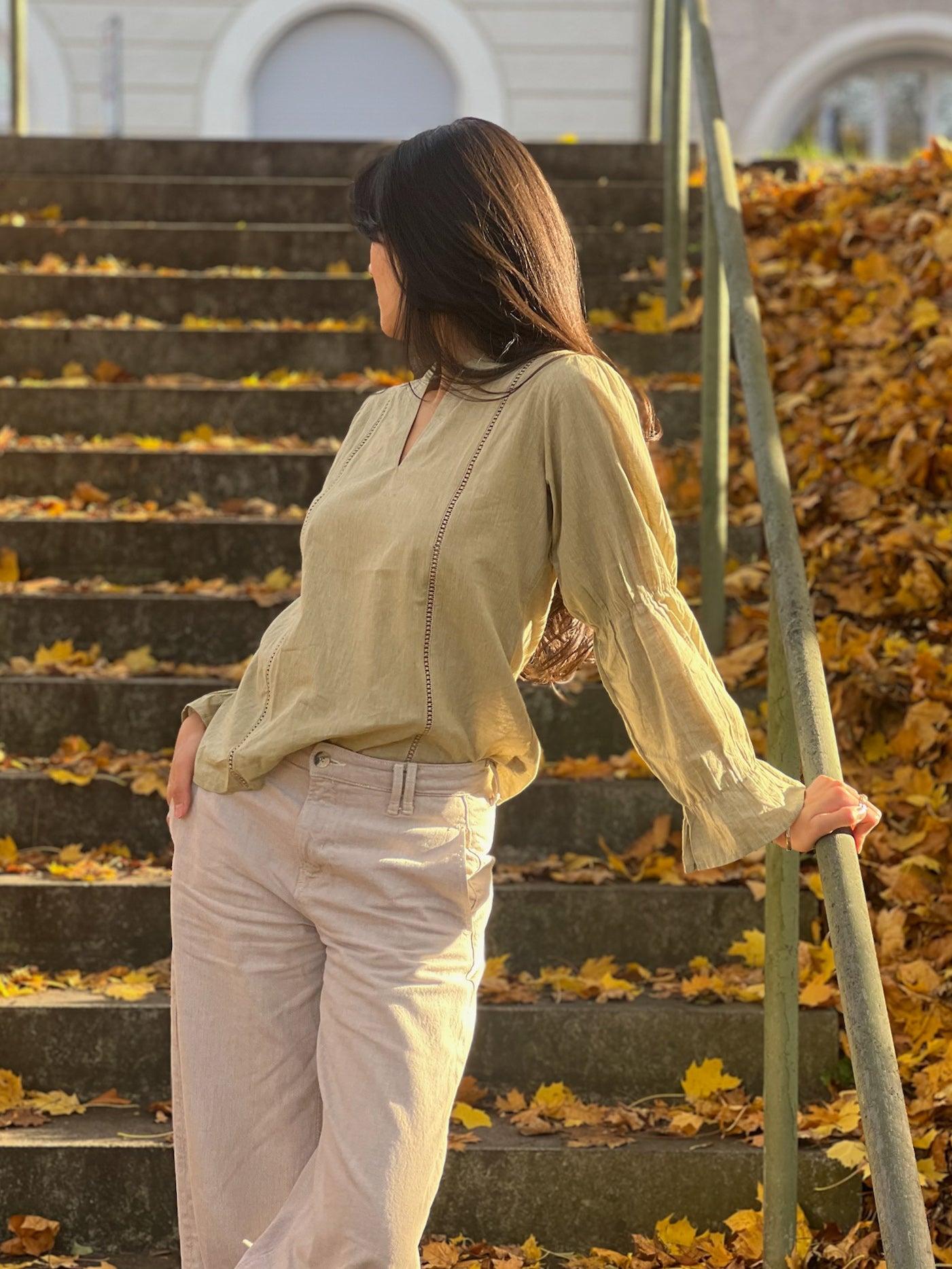 Woman standing on a leaf-covered staircase holding a green garden tool.
