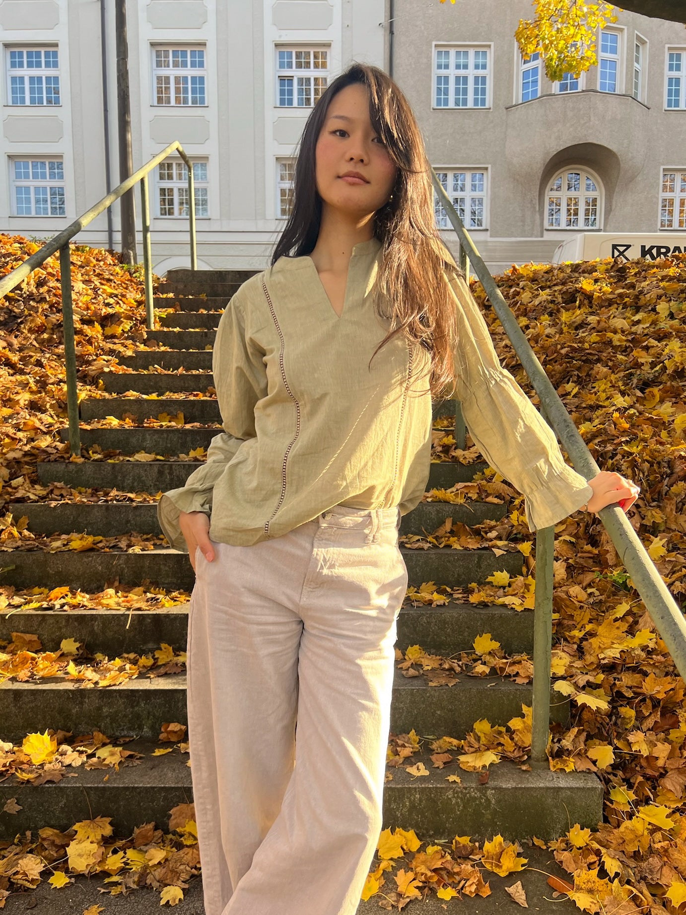 Woman standing on a staircase with autumn leaves and a building in the background