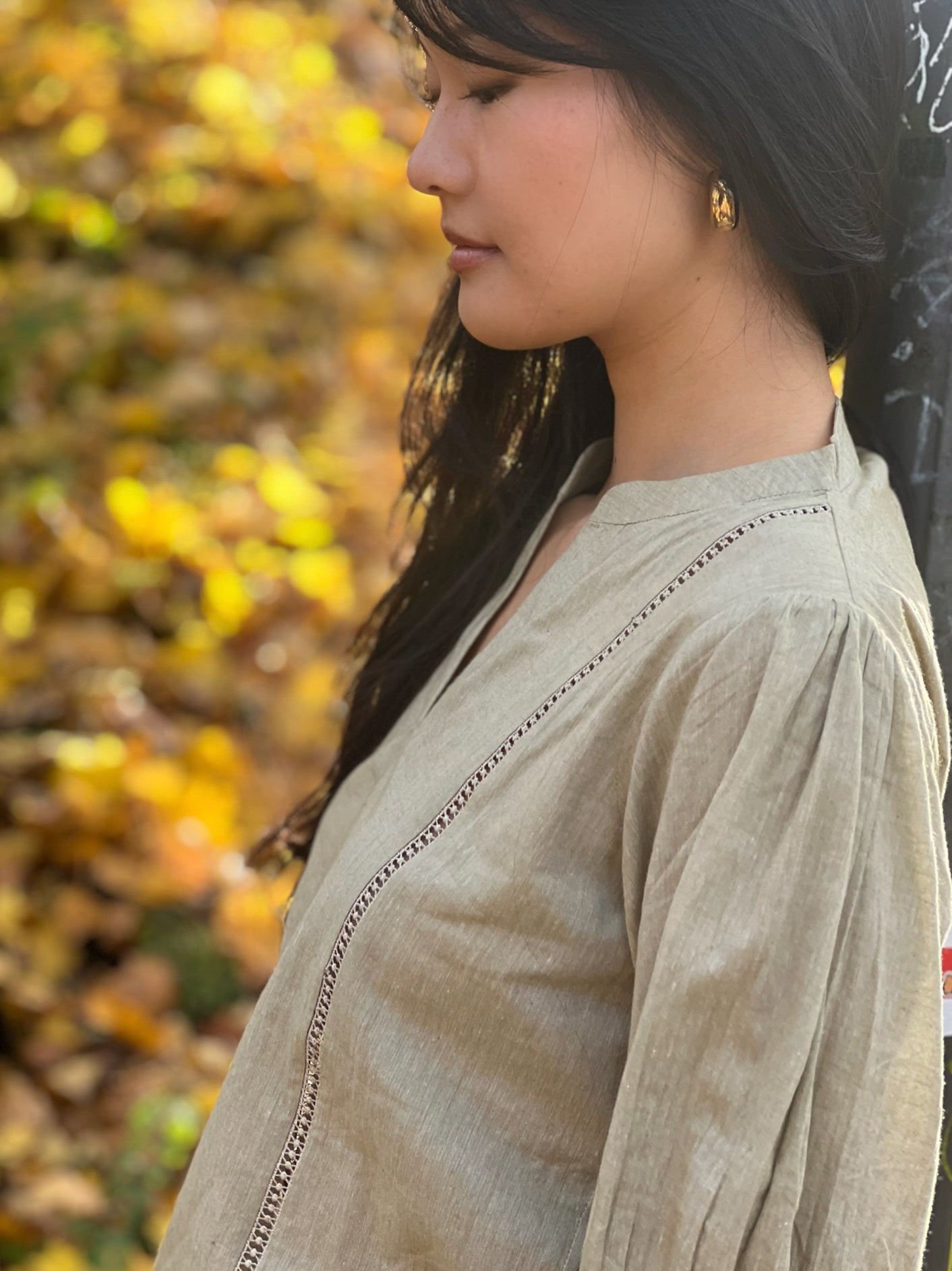 Woman wearing a beige top with a blurred autumn leaf background