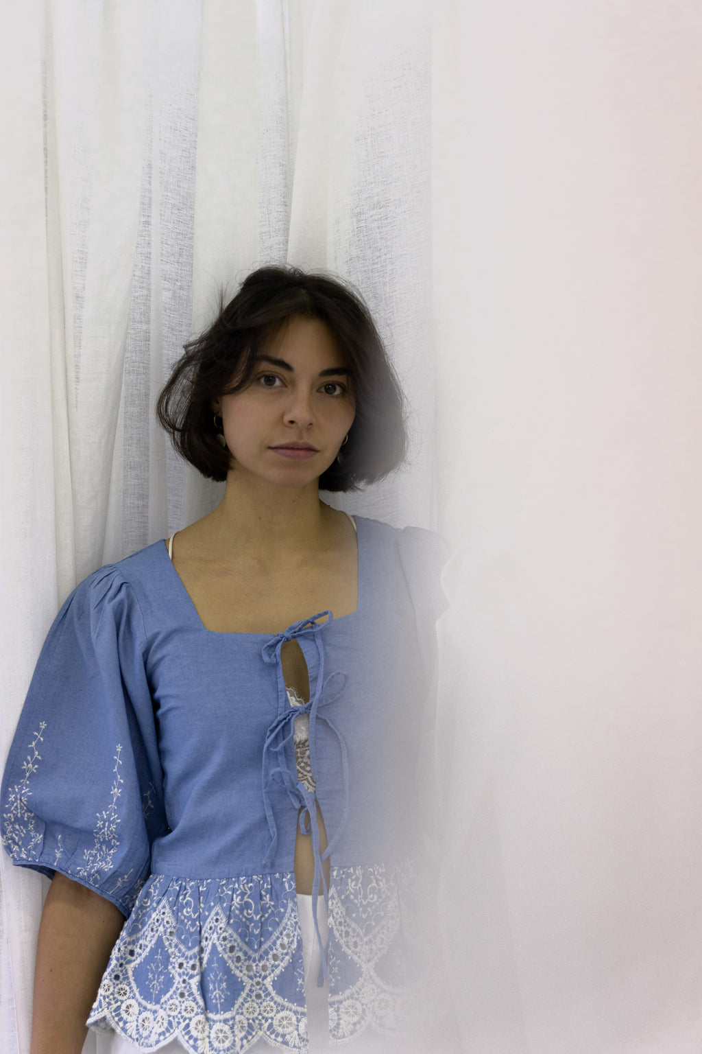 Muse denim blouse with white embroidery, puffy sleeves, and bow-tie details
