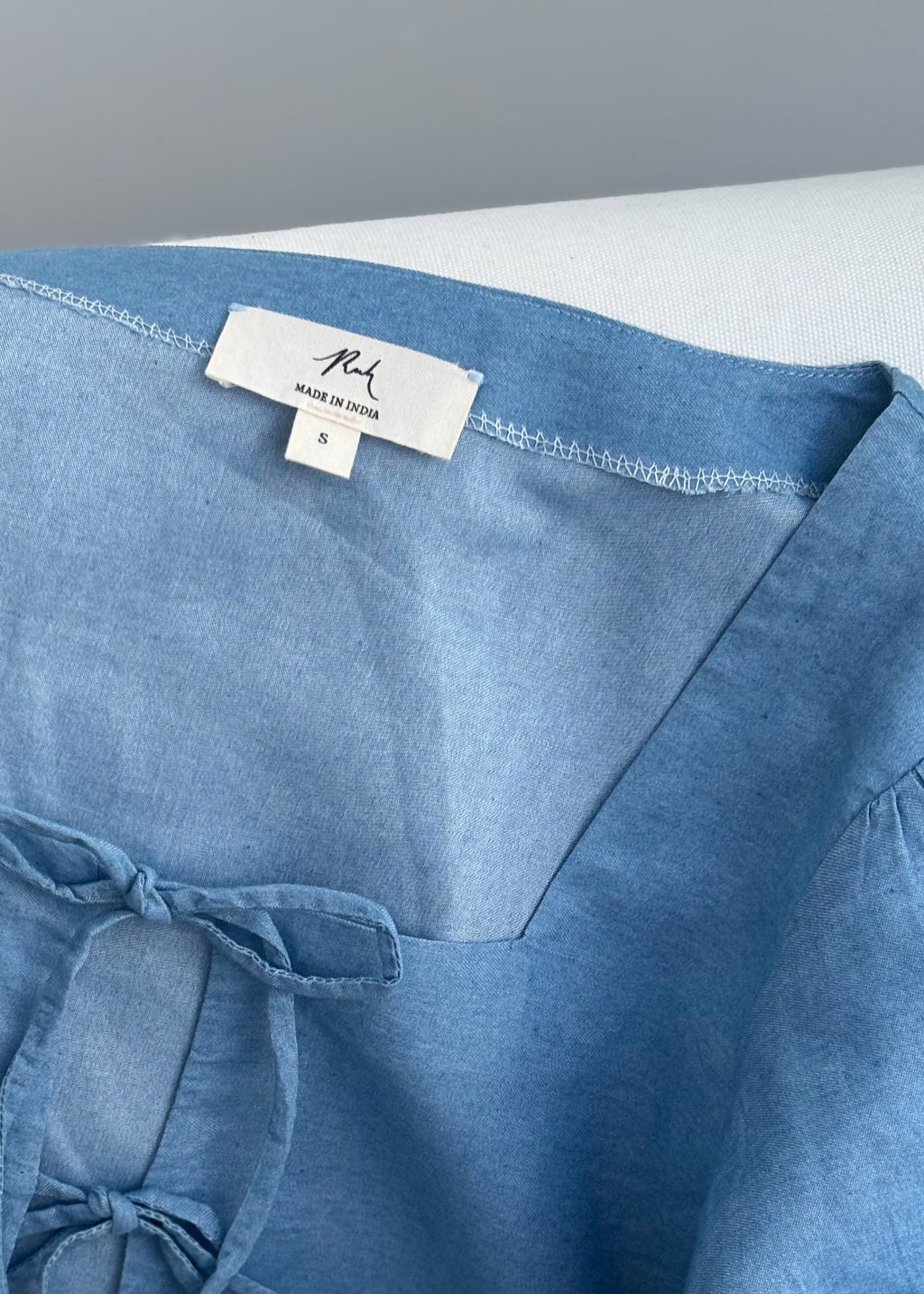 Muse denim blouse with white embroidery, puffy sleeves, and bow-tie details
