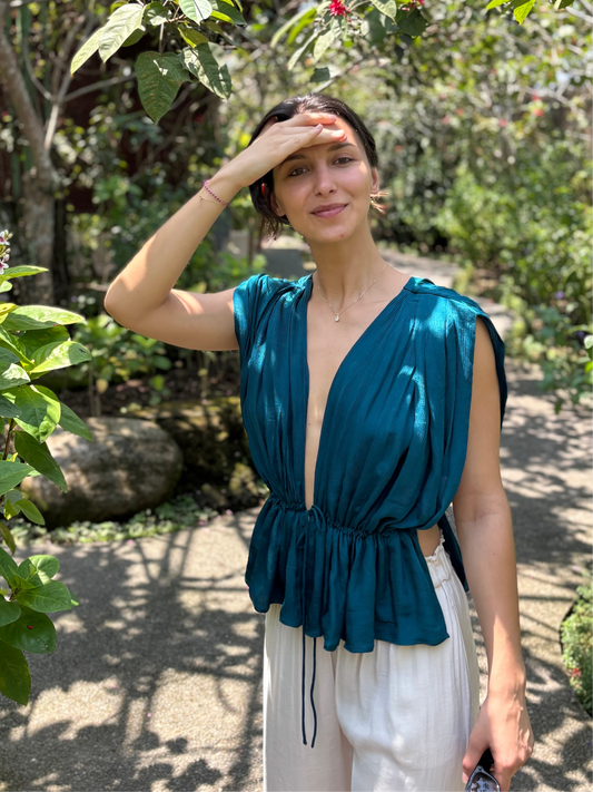 Woman in a teal top and white pants standing in a garden