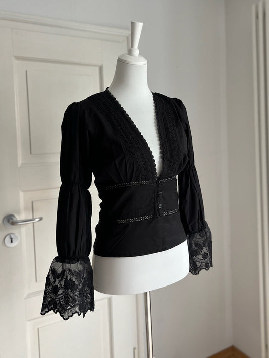 Black blouse with lace cuffs on a mannequin against a white door. RUH Allure Blouse styled for modern women – refined slow fashion with cultural soul and natural comfort. 