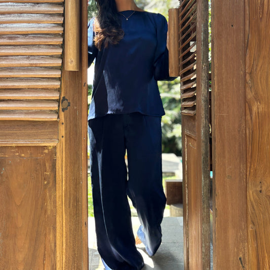 Person wearing a navy blue outfit standing in a doorway with wooden slats. 